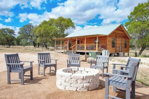 A wooden cabin with a porch, surrounded by outdoor seating and a stone fire pit.
