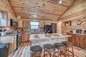 A wooden cabin-style kitchen with a central island, bar stools, and a refrigerator.