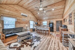 Interior de una cabaña con techo de madera, un sofá de cuero negro, una mesa de comedor y una zona de cocina.