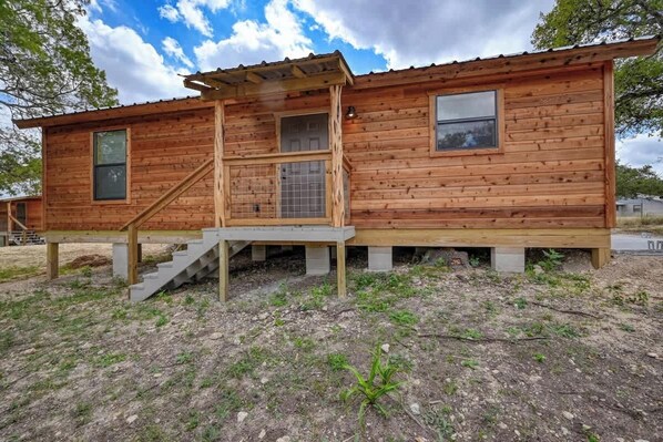A wooden cabin with a front porch, a staircase, and a small window.