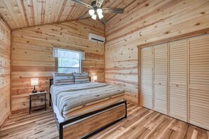 A wooden-paneled bedroom with a bed, bedside lamps, a window, and a closet.