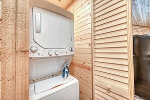 A compact laundry area with a washing machine and dryer, wooden walls, and a visible door leading to another room.