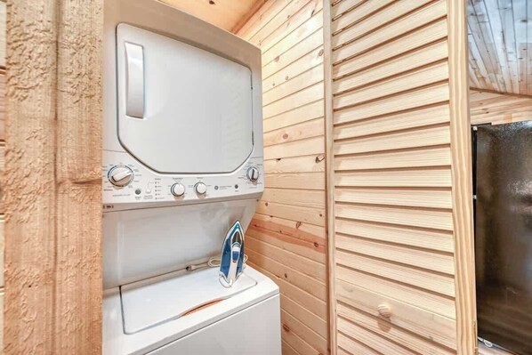A compact laundry area with a washing machine and dryer, wooden walls, and a visible door leading to another room.