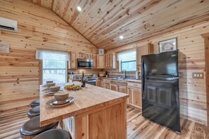 Cocina de cabaña de madera con una isla central, un refrigerador negro y armarios de madera.