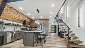 A modern kitchen with a central island, stainless steel appliances, and a wooden accent wall. - Luxury A-Frame*Hot-tub*Firepit (Omaha)