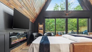 A modern bedroom with a large bed, a fireplace, and a TV. - Luxury A-Frame*Hot-tub*Firepit (Omaha)
