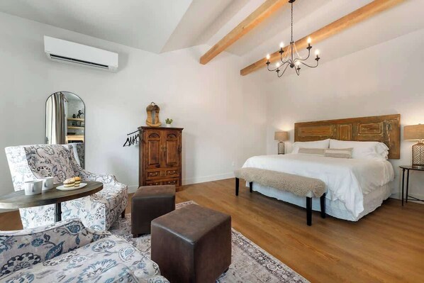 A bedroom with a large bed, a wooden headboard, a chandelier, a wardrobe, and a mirror.