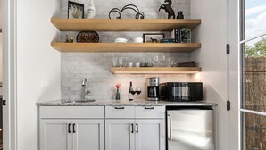 Una cocina con armarios blancos, un refrigerador de acero inoxidable, un microondas y estantes de madera arriba.
