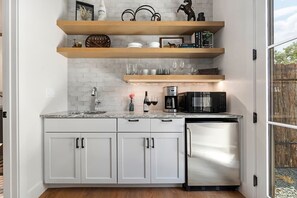 A kitchen with white cabinets, a stainless steel refrigerator, a microwave, and wooden shelves above.