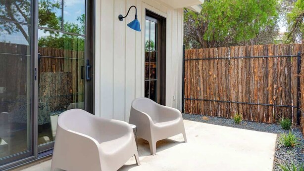 Un patio moderno al aire libre con dos sillas blancas y una lámpara azul fijada a la pared.