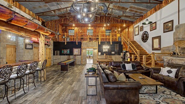 A rustic interior with a wooden ceiling, a chandelier, a staircase, and a bar area.