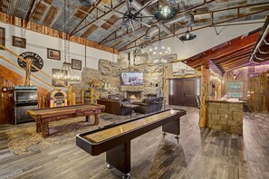 Interior rústico com mesa de bilhar, área de estar, parede de pedra e lareira.