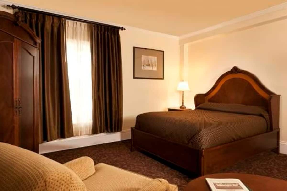 A hotel room with a bed, a chair, a lamp, and a framed picture on the wall.