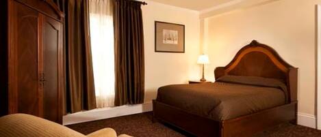 A hotel room with a bed, a chair, a lamp, and a framed picture on the wall.