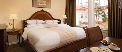A hotel room with a bed, bedside lamps, a dining table with a book and glasses, and a window with curtains.