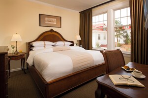 Una camera d'albergo con un letto, abat-jour, un tavolo da pranzo con un libro e dei bicchieri, e una finestra con tende.