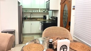 A compact kitchen with white cabinets, a black stove, and a sink. There is a wicker chair and a table with woven placemats.