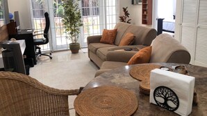 A living room with a sofa, a coffee table, a potted plant, and a television on the wall.