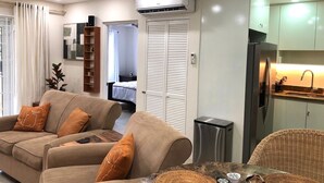 A modern living room with a sofa set, a dining table, and a kitchen area with a refrigerator and sink.