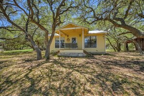 Une maison jaune avec un porche, entourée d’arbres.