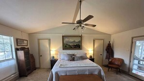 Un dormitorio con una cama, un banco de madera, un ventilador de techo, un aparador y una ventana.