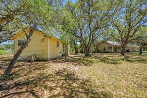 A yellow house with a porch, surrounded by trees and a grassy yard.