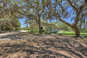 A two-story house with a porch, surrounded by trees and a well-maintained lawn. - 45-ac Estate-Private Blanco River Access-Fire Pit! (Blanco)