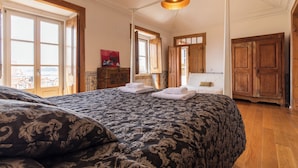 Une chambre avec un grand lit, une armoire en bois et une vue sur la mer, accessible par une porte-fenêtre donnant sur un balcon.