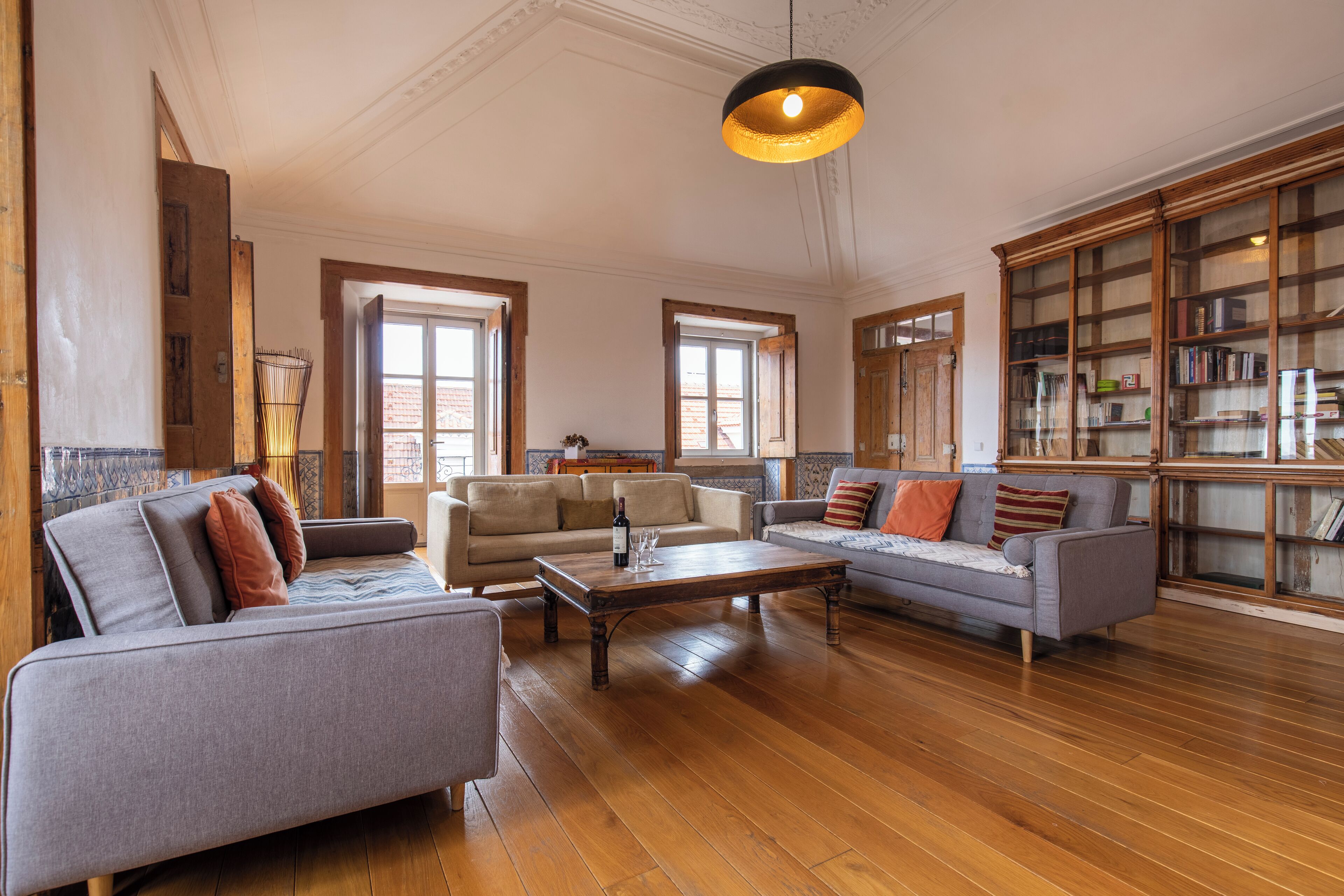 A spacious living room with hardwood flooring, a large bookshelf, and two sofas with cushions.