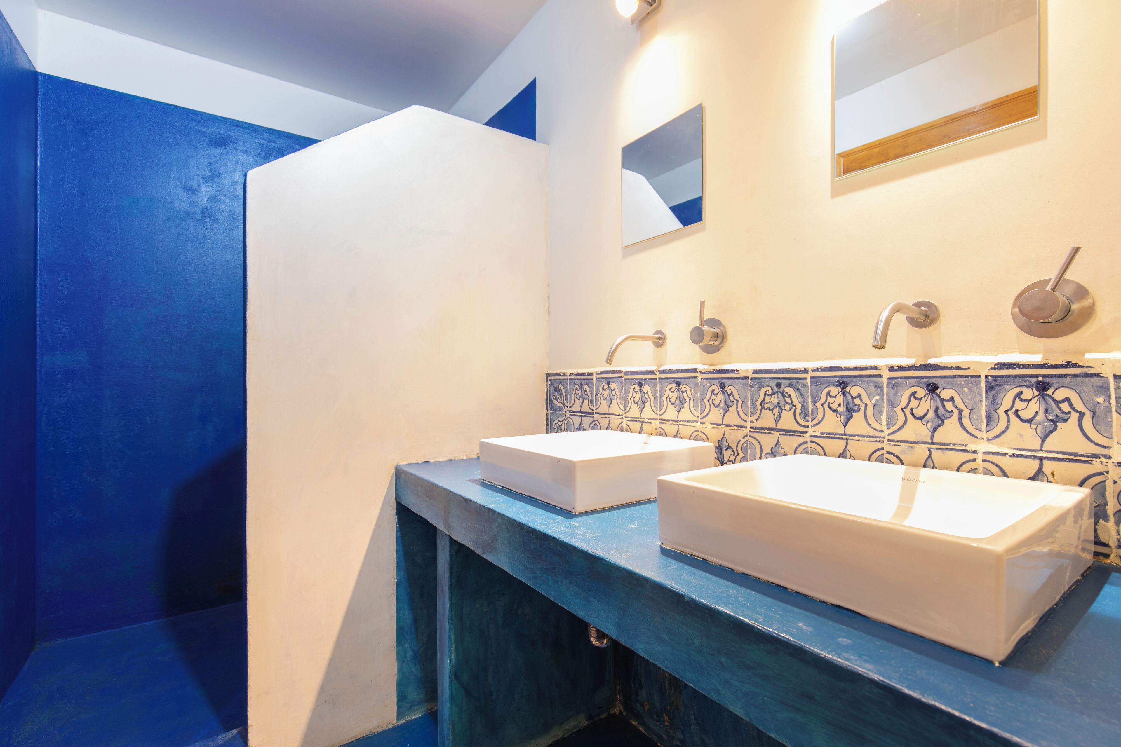 A bathroom with two white sinks, a blue vanity, and a decorative tile backsplash.