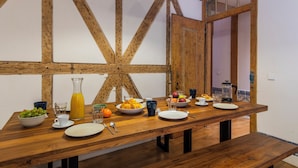 Une table de salle à manger en bois, mise pour le petit-déjeuner, avec une carafe de jus d’orange et une machine à café.