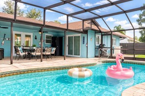 Una piscina exterior techada con zona de patio, una mesa con sillas y un flotador con forma de flamenco.