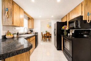 Une cuisine avec des meubles de rangement en bois, un réfrigérateur noir, un four à micro-ondes et une cuisinière.