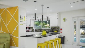 A modern kitchen with white cabinets, a black countertop, and yellow stools. - Golden Vibes • Fun for Everyone (Bradenton)