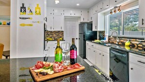A modern kitchen with white cabinets, a black refrigerator, and a wooden countertop with a variety of food items and bottles. - Golden Vibes • Fun for Everyone (Bradenton)