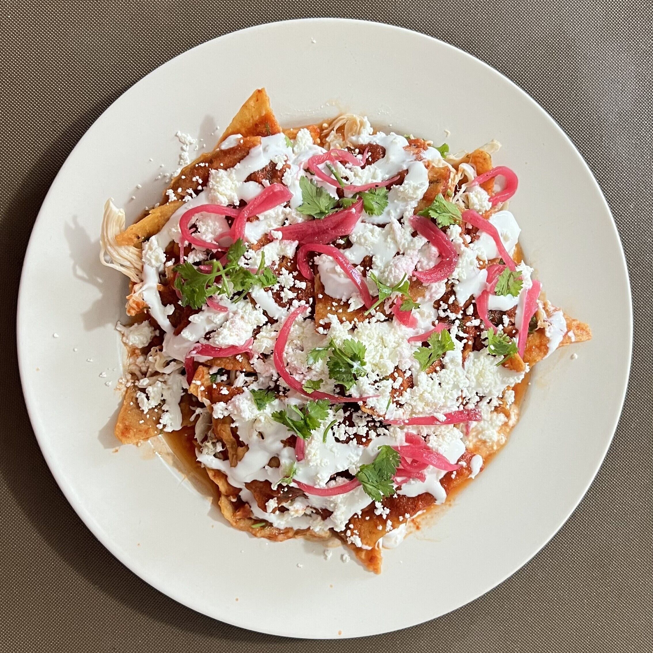 A plate of nachos topped with cheese, sour cream, and red onions.