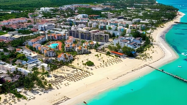 An aerial view of a coastal resort with a beach, buildings, and a clear view of the ocean. - Condo in Epic Punta Cana! Near Cocobongo (Punta Cana)