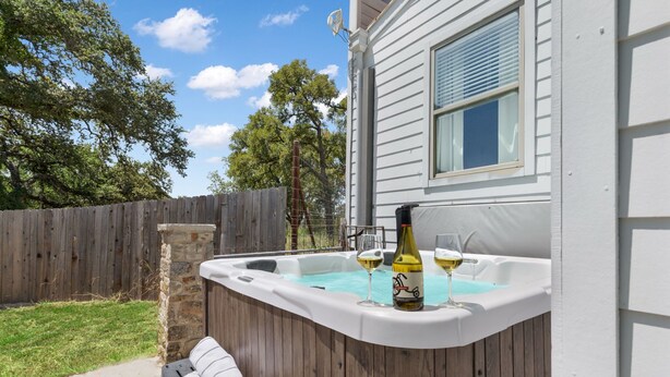 Ein Whirlpool mit zwei Gläsern Weißwein und einer Flasche, eine Steinmauer und ein Holenzaun im Hintergrund.