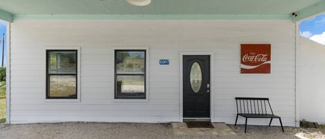 A white building with a black door, a Coca-Cola sign, and a bench outside.