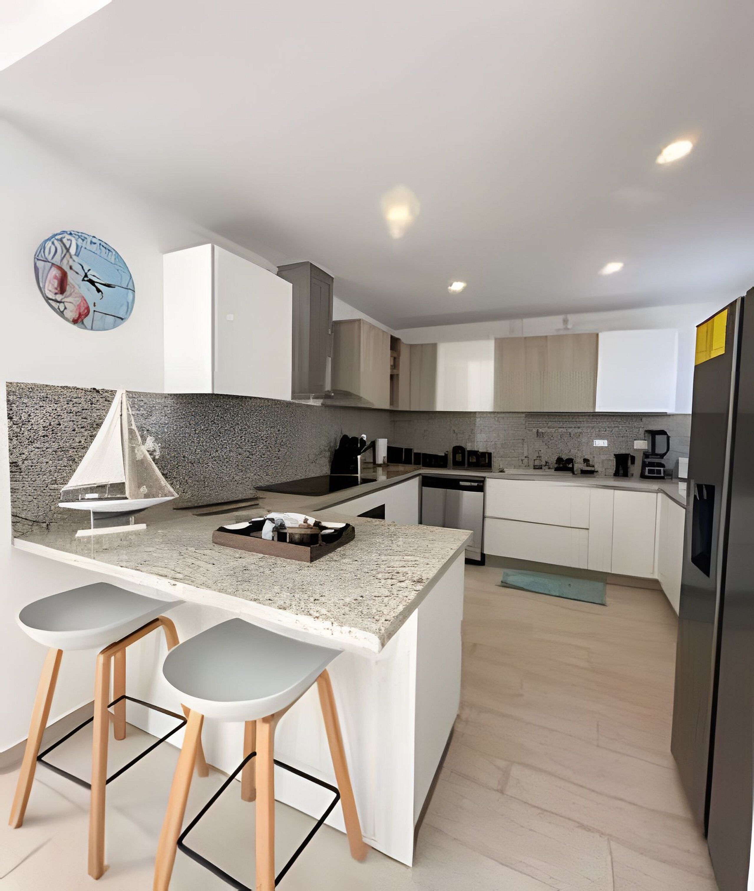 A modern kitchen with a central island, bar stools, a clock, and a coffee machine.