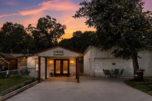 A house with a 'HOME' sign, a covered porch, a garage, and a patio with chairs.