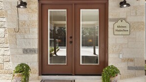 A double wooden door with glass panels, a stone wall, and two potted plants.