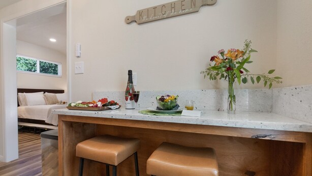 A modern kitchen with a wooden bar counter, stools, a 'KITCHEN' sign, and a vase with flowers.