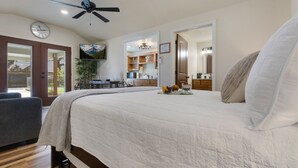 A bedroom with a large bed, a ceiling fan, a clock, and a view of the outside.