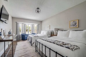A bedroom with two beds, a desk, a chair, a TV, and a window with curtains.