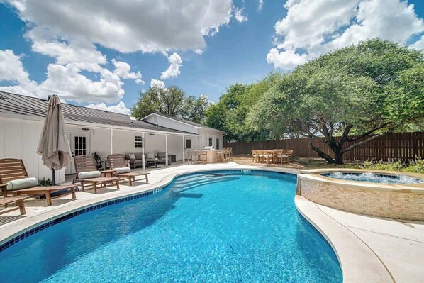 A backyard with a swimming pool, lounge chairs, and a covered patio area.