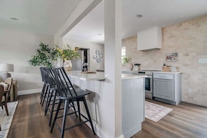 A modern kitchen with white cabinetry, a central island, and a dining area with black bar stools.