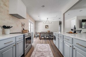 A modern kitchen with light blue cabinets, a central island, and a dining area with wooden chairs.