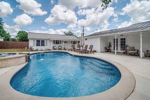 A backyard with a swimming pool, lounge chairs, and a covered patio area.