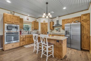 A kitchen with wooden cabinets, stainless steel appliances, a central island with bar stools, and a ceiling with recessed lighting.